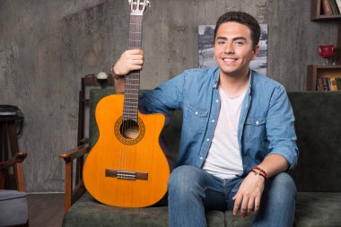 Genç bir müzisyen güzel bir gitar tutuyor ve kanepede oturuyor. Yüksek kalite fotoğraf