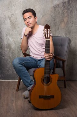 Sandalyede oturan ve gitarı tutan genç bir adam. Yüksek kalite fotoğraf