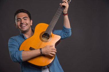 Genç müzisyen siyah arka planda gitar çalıyor.