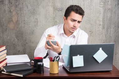 Ofis çalışanı dizüstü bilgisayara bakıyor ve büro masasında telefonu tutuyor. Yüksek kalite fotoğraf