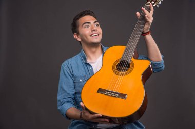 Mutlu adam karanlık arka planda yeni gitarına bakıyor. Yüksek kalite fotoğraf