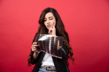 Kırmızı arka planda fotoğraf kaseti olan bir dosyaya bakan genç bir kadın. Yüksek kalite fotoğraf