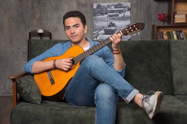 Gülümseyen müzisyen gitar çalıp koltukta oturuyor. Yüksek kalite fotoğraf