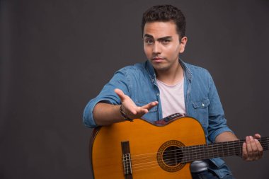 Gitarlı genç adam karanlık arka planda şaşkın görünüyor. Yüksek kalite fotoğraf