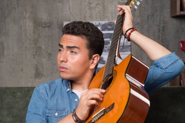 Genç bir müzisyen güzel bir gitar tutuyor ve kanepede oturuyor. Yüksek kalite fotoğraf