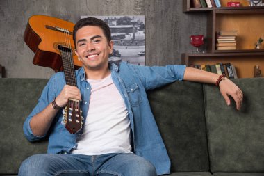 Neşeli müzisyen elinde güzel bir gitarla kanepede oturuyor. Yüksek kalite fotoğraf