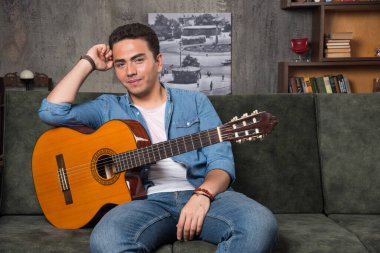 Genç gitarist elinde güzel bir gitaristle kanepede oturuyor. Yüksek kalite fotoğraf