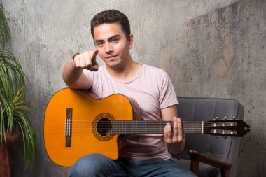 Kamerayı gösteren ve sandalyede gitar tutan bir adam. Yüksek kalite fotoğraf