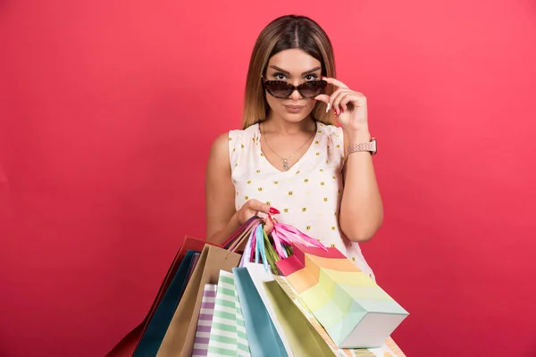 Frau Trägt Einkaufstüten Während Sie Ihre Brille Auf Rotem Hintergrund — Stockfoto