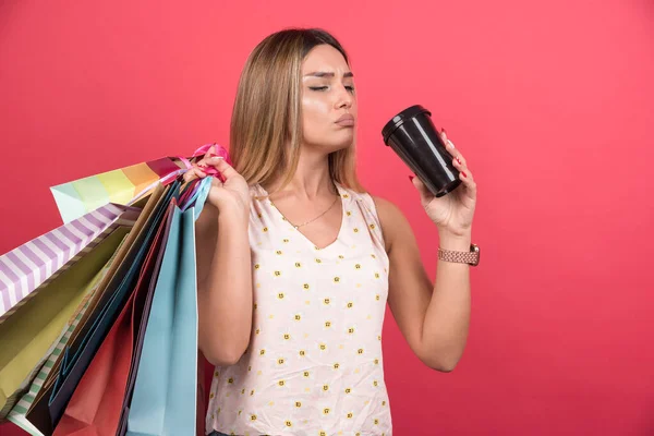 Vrouw Die Haar Boodschappentassen Vasthoudt Koffie Drinkt Een Rode Achtergrond — Stockfoto