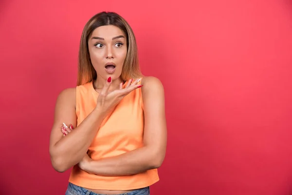 Mujer Joven Confundida Señalando Mano Lado Sobre Fondo Rojo Foto — Foto de Stock