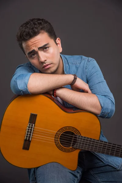 ギターを背景に若い男が座って疲れている 高品質の写真 — ストック写真