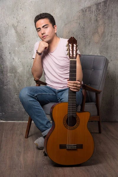 若い男が椅子に座ってギターを持っている 高品質の写真 — ストック写真