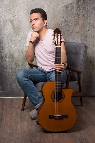 ギターを持ちながら椅子に座っているハンサムな若い男 高品質の写真 — ストック写真