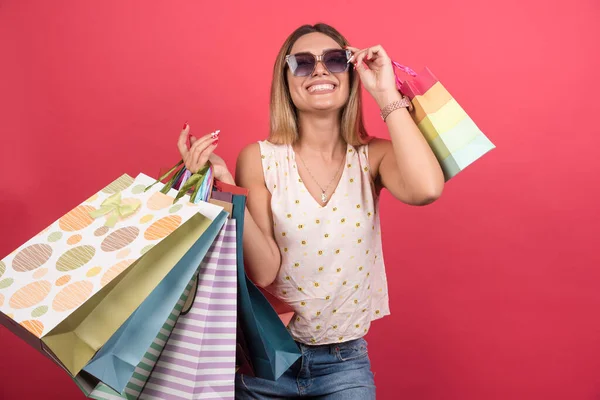 Frau Trägt Einkaufstüten Während Sie Ihre Brille Auf Rotem Hintergrund — Stockfoto