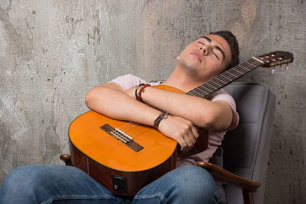 ギターを持って椅子の上で寝ているハンサムな若い男 高品質の写真 — ストック写真