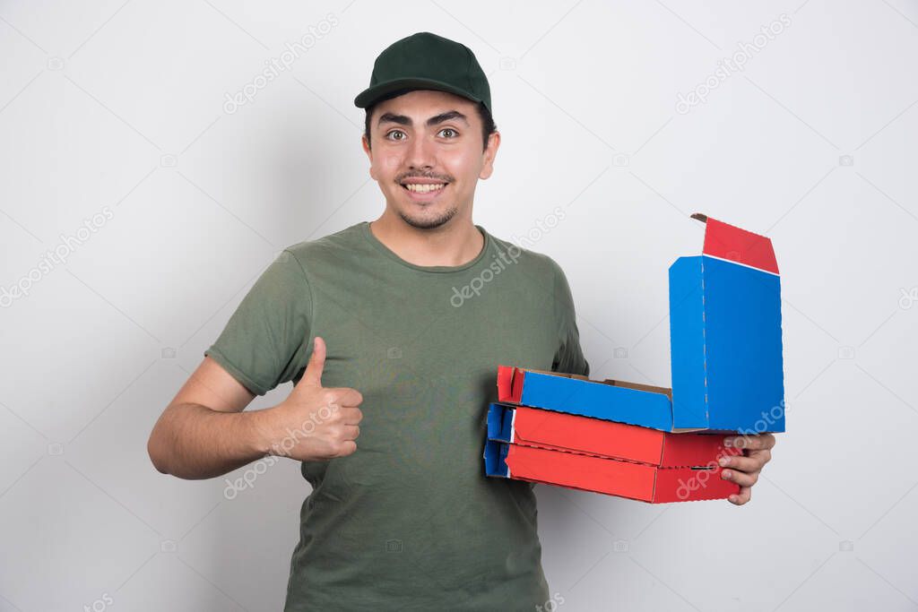 Deliveryman showing thumbs up and carrying pizza boxes on white background. High quality photo