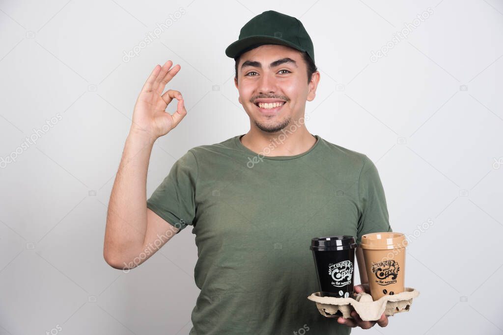 Delivery man holding takeaway cups of coffees on white background. High quality photo