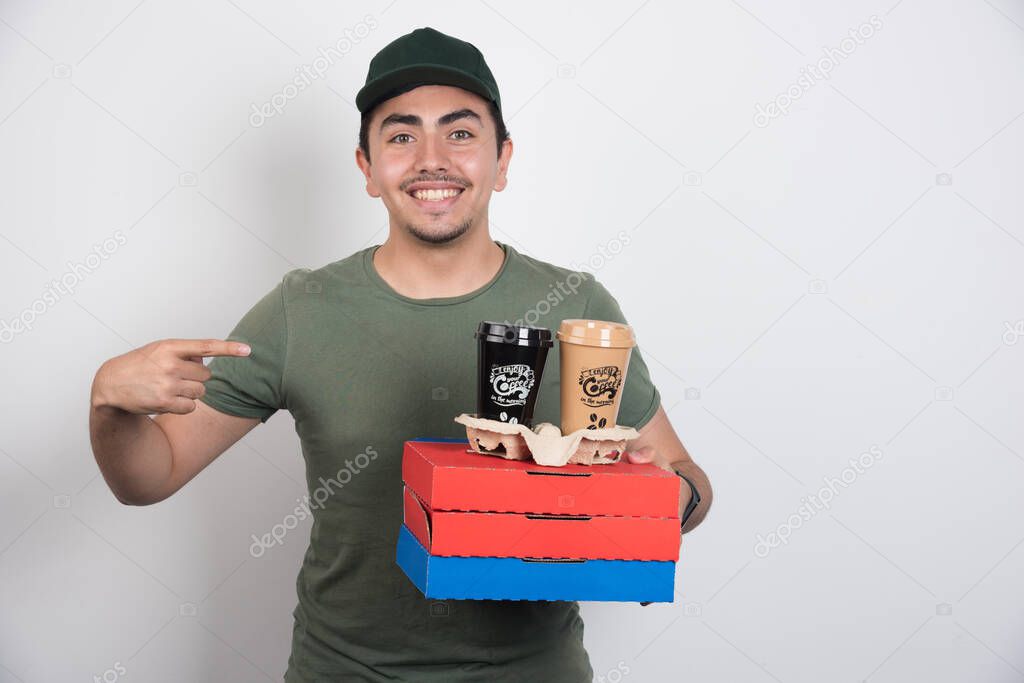 Deliveryman pointing at three boxes of pizza and coffees on white background. High quality photo