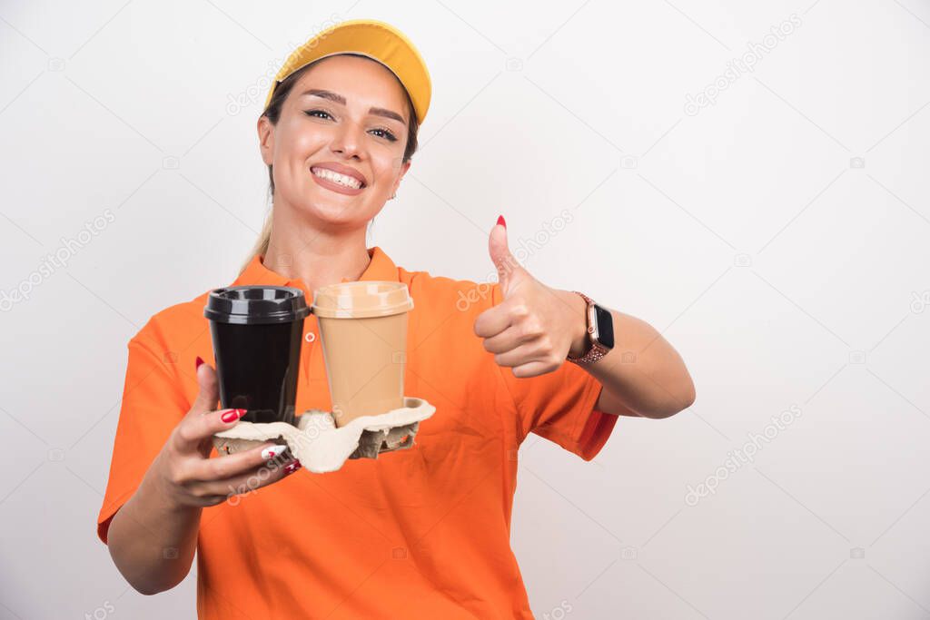 Woman courier holding two cups of coffees making thumbs up sign on white background. High quality photo