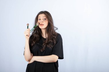 Beyaz arka planda fırçayla makyaj yapan genç modelin portresi. Yüksek kalite fotoğraf