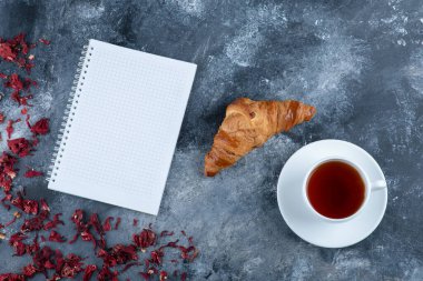 Taze ve lezzetli kruvasan, bir fincan sıcak çay ve defter. Yüksek kalite fotoğraf