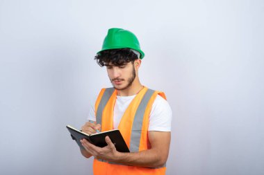 Beyaz duvarın üzerinde deftere yazılı, kasketli yakışıklı erkek mühendis. Yüksek kalite fotoğraf