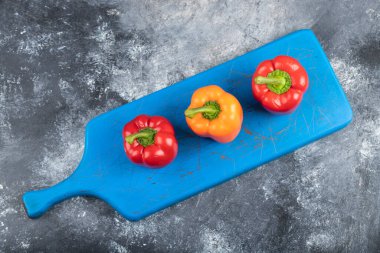 Three fresh organic colorful bell peppers on blue cutting board. High quality photo