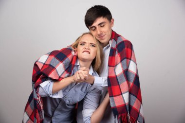 Gri arka planda, genç ve güzel bir çift sıcak bir battaniyeye sarılır. Yüksek kalite fotoğraf