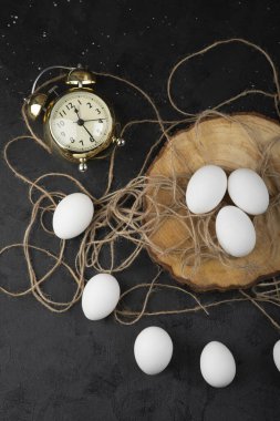 Ahşap parçasında üç beyaz çiğ yumurta ve siyah zemin üzerinde çalar saat. Yüksek kalite fotoğraf