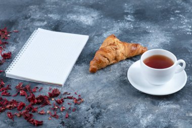 Mermer bir masaya beyaz bir fincan sıcak çay konulmuş sade kruvasan. Yüksek kalite fotoğraf