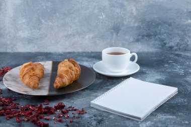 Bir fincan kruvasanla çay ve taş masaya yerleştirilmiş bir defter. Yüksek kalite fotoğraf