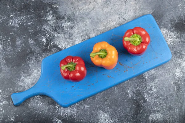 Three fresh organic colorful bell peppers on blue cutting board. High quality photo