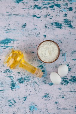 İki taze tavuk yumurtası ve ahşap bir kase unla birlikte bir şişe yağ. Yüksek kalite fotoğraf