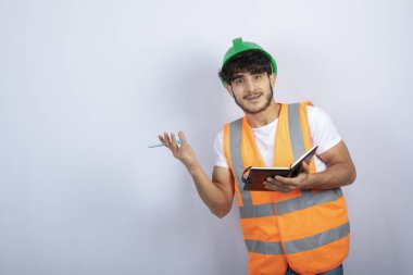 Beyaz duvarın üzerinde duran yeşil şapkalı yakışıklı erkek mühendis. Yüksek kalite fotoğraf