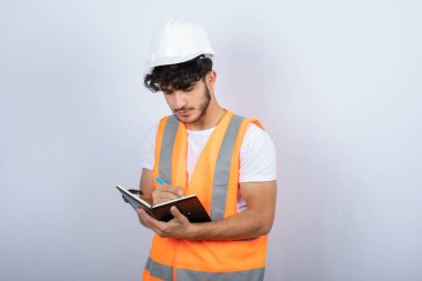 Beyaz duvarın üzerinde deftere yazılı, kasketli yakışıklı erkek mühendis. Yüksek kalite fotoğraf