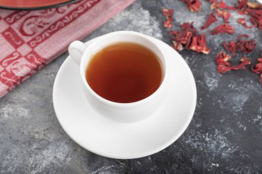 White cup of hot black tea with dried flower buds placed on a dark grey background . High quality photo
