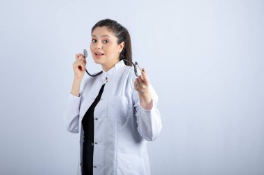 Beyaz önlüklü güzel doktor beyaz duvarın üzerinde duruyor ve poz veriyor. Yüksek kalite fotoğraf