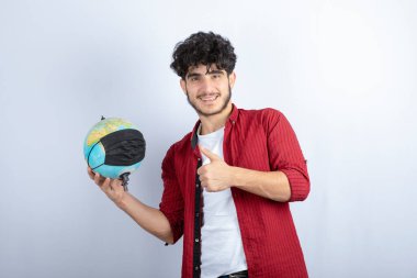 Genç adam, elinde tıbbi maskeli bir toprak küresi tutuyor ve baş parmağını kaldırıyor. Yüksek kalite fotoğraf