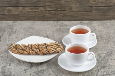 Üzerine tohum serpiştirilmiş taze yulaf ezmeli kurabiyeler ve iki fincan siyah çay. Yüksek kalite fotoğraf