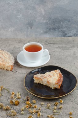 Lezzetli bir pastanın siyah tabağı ve arka planda beyaz bir fincan sıcak çay. Yüksek kalite fotoğraf