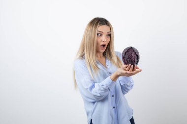 Mavi elbiseli güzel kadın beyaz arka planda mor lahanaya bakıyor. Yüksek kalite fotoğraf
