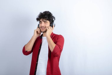 Kulaklıklı yakışıklı bir gencin beyaz duvarda şarkı dinlediği bir görüntü. Yüksek kalite fotoğraf