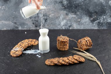 Kadın eli, siyah arka planda kurabiyeli süt şişesine süt döküyor. Yüksek kalite fotoğraf