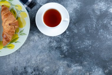 Renkli bir tabak taze kruvasan ve mermer arka planda beyaz bir fincan sıcak çay. Yüksek kalite fotoğraf