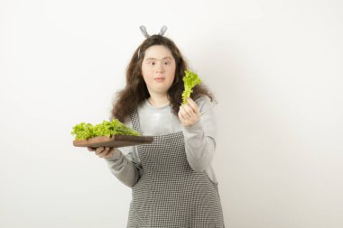 Kıvırcık saçlı, tahta marul yaprakları tutan genç bir kızın fotoğrafı. Yüksek kalite fotoğraf