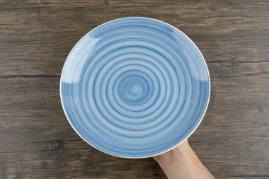 Ahşap bir masada boş mavi bir tabak tutan erkek elleri. Yüksek kalite fotoğraf