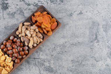 Tahta tabak dolusu fındık, kraker ve mermer yüzeyde kurutulmuş kayısı. Yüksek kalite fotoğraf