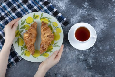 Kadın eli, bir fincan çayın yanında taze pişmiş kruvasan tabağı tutuyor. Yüksek kalite fotoğraf