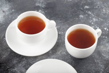 Two white cups of hot black tea placed on a dark grey background . High quality photo